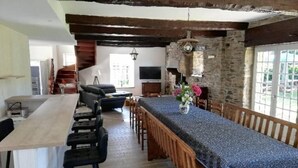 A rustic dining area with a long table, wooden chairs, and a stone wall.