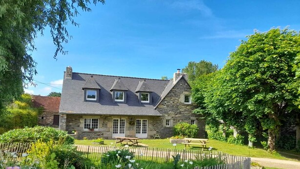 A stone house with a sloped roof, a fenced garden, and a picnic table.