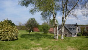 A stone house with a sloped roof, surrounded by a well-maintained lawn and mature trees.