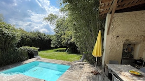 Eine Holzterrasse mit Pool, einem Esstisch und einem gelben Sonnenschirm.