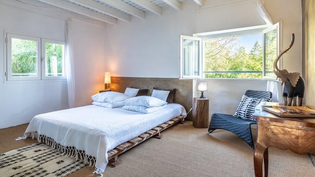 Ein Schlafzimmer mit Bett, Stuhl, Tisch und einem Fenster mit Blick ins Grüne.