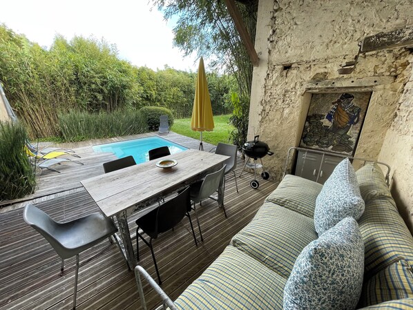 A wooden deck with a pool, outdoor seating, and a grill.