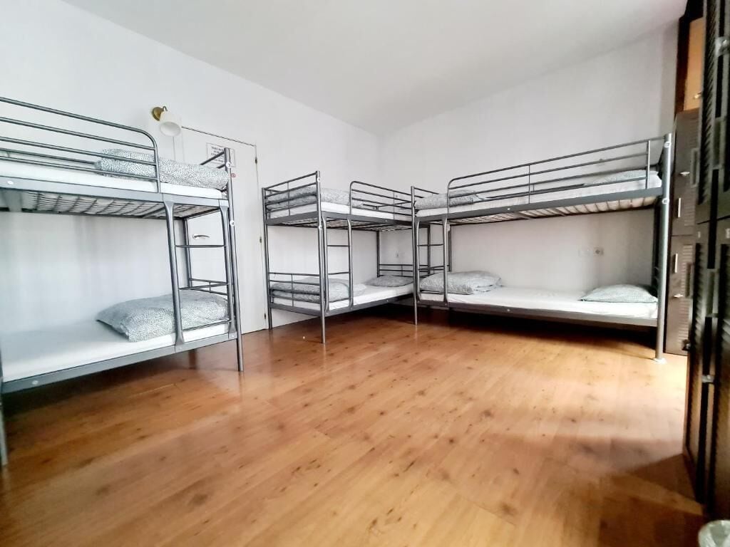 A room with four bunk beds arranged in a corner, wooden flooring, and a white wall.