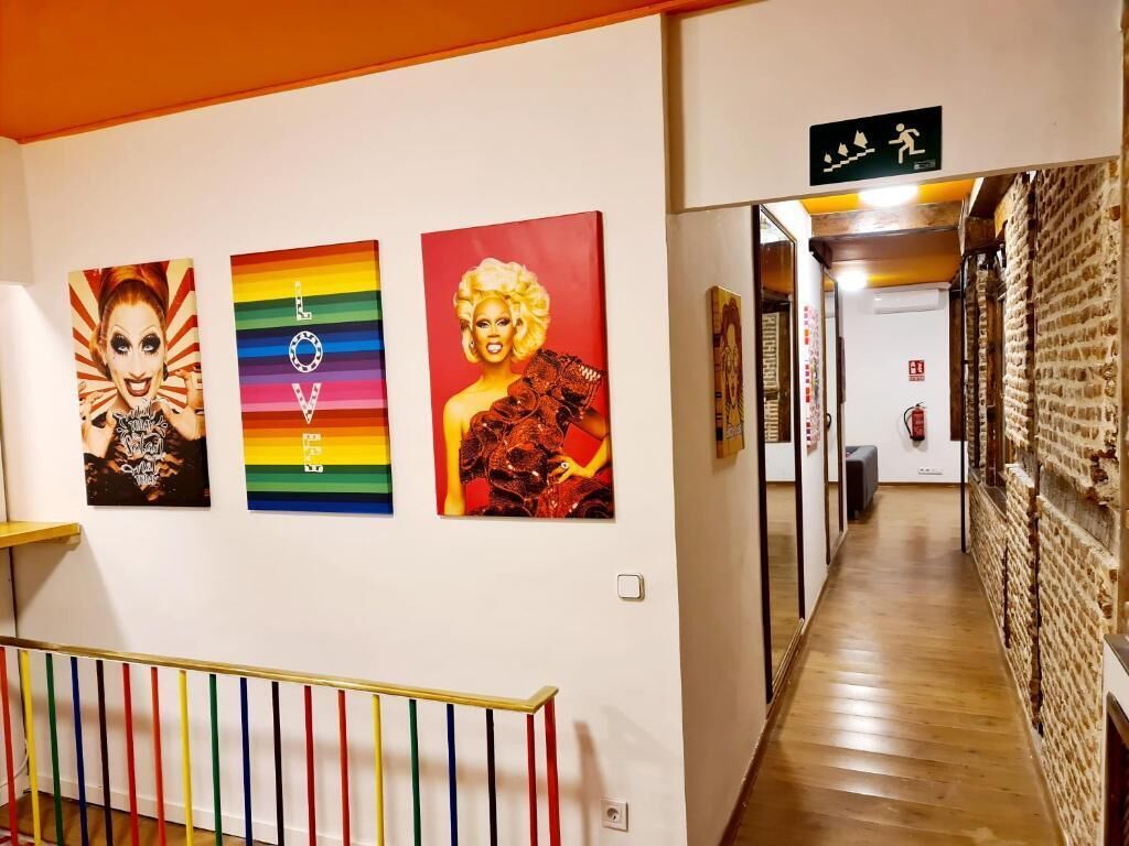 A hallway with a staircase, a fire exit sign, and three colorful artworks on the wall.