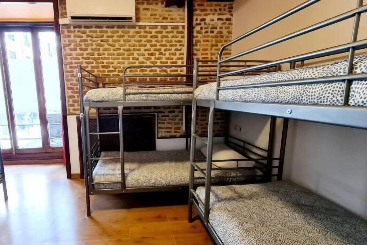 Quarto com beliche, parede de pedra, janela com cortinas vermelhas e aparelho de ar condicionado.