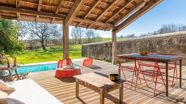 Eine Holzterrasse mit Pool, roten Stühlen und einem Tisch.