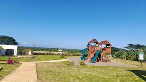 Une aire de jeux avec des toboggans et des structures d’escalade, entourée d’une pelouse et d’un bâtiment.