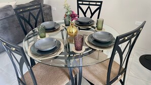 Une table de salle à manger ronde en verre, entourée de chaises noires, d’un canapé gris et d’une chaise noire dotée d’un dossier à motifs géométriques.