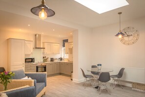 A modern kitchen with white cabinets, a dining area with a glass table and metal chairs, and a skylight above.