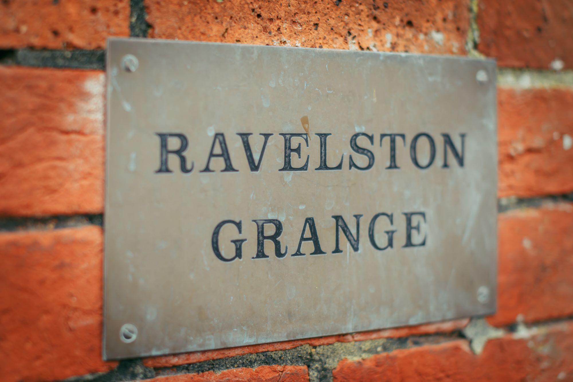 Un letrero de metal con el texto "RAVELSTON GRANGE" sujeto a una pared de ladrillo.