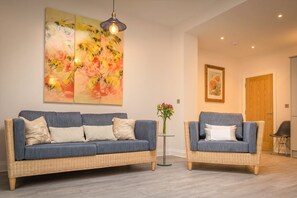 A living room with two wicker sofas, a glass coffee table, and a large abstract painting on the wall.