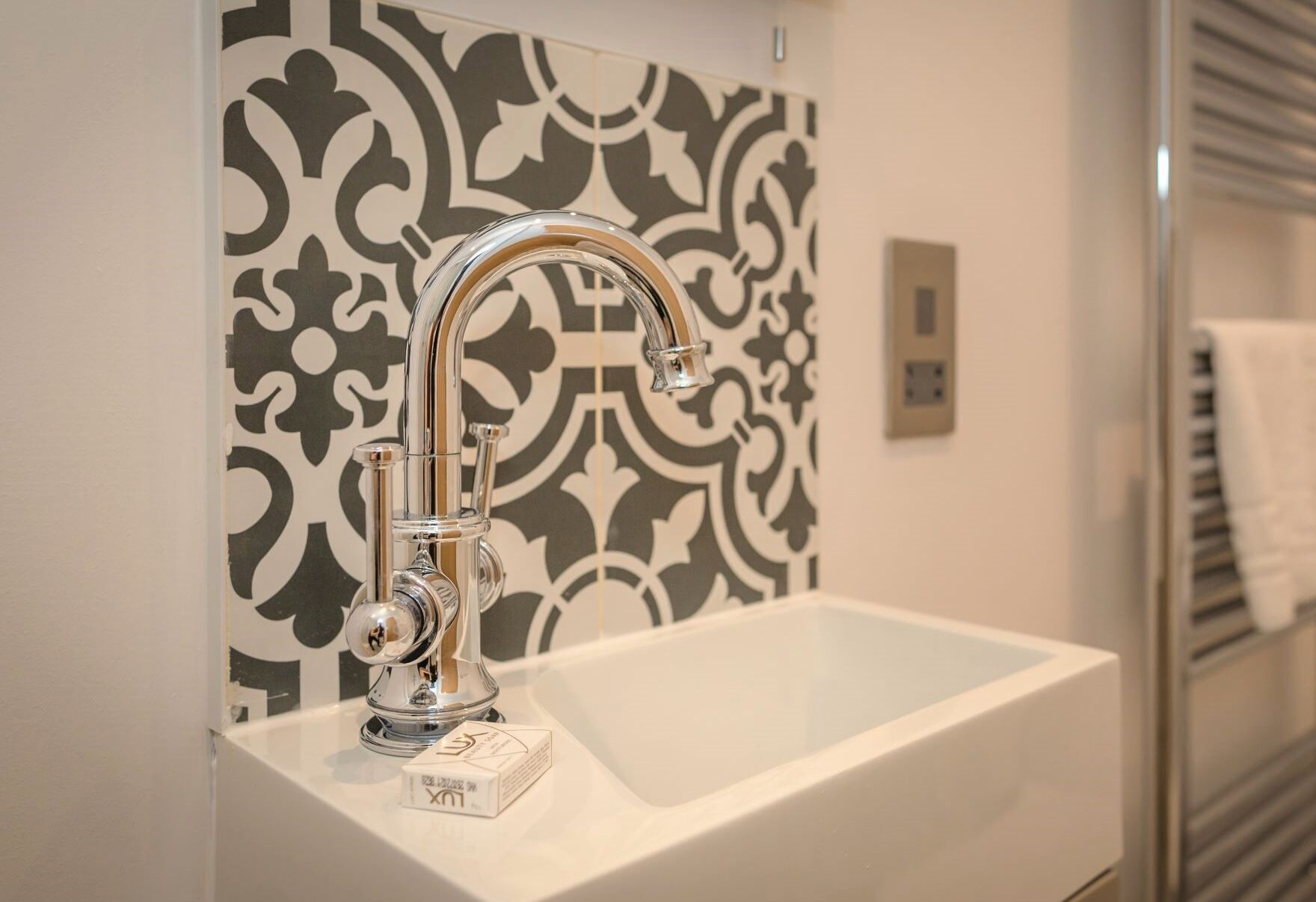A bathroom with a modern sink and faucet, a patterned wall, and a towel rack.
