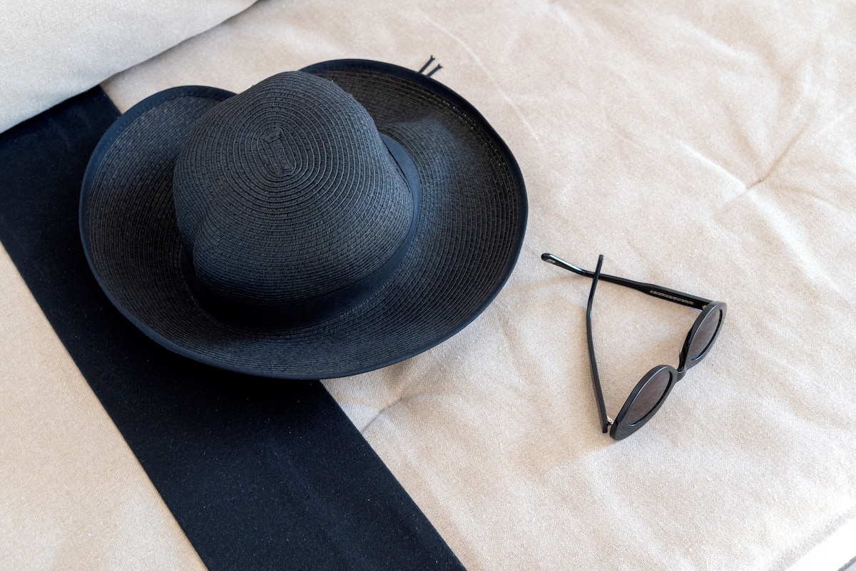 A black hat and sunglasses on a beige fabric surface.