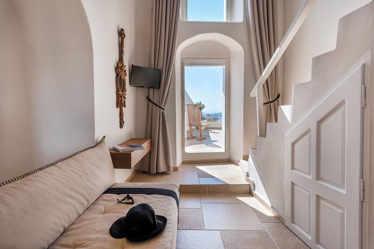 A hotel room with a bed, a TV, a window with curtains, and a view of the beach.