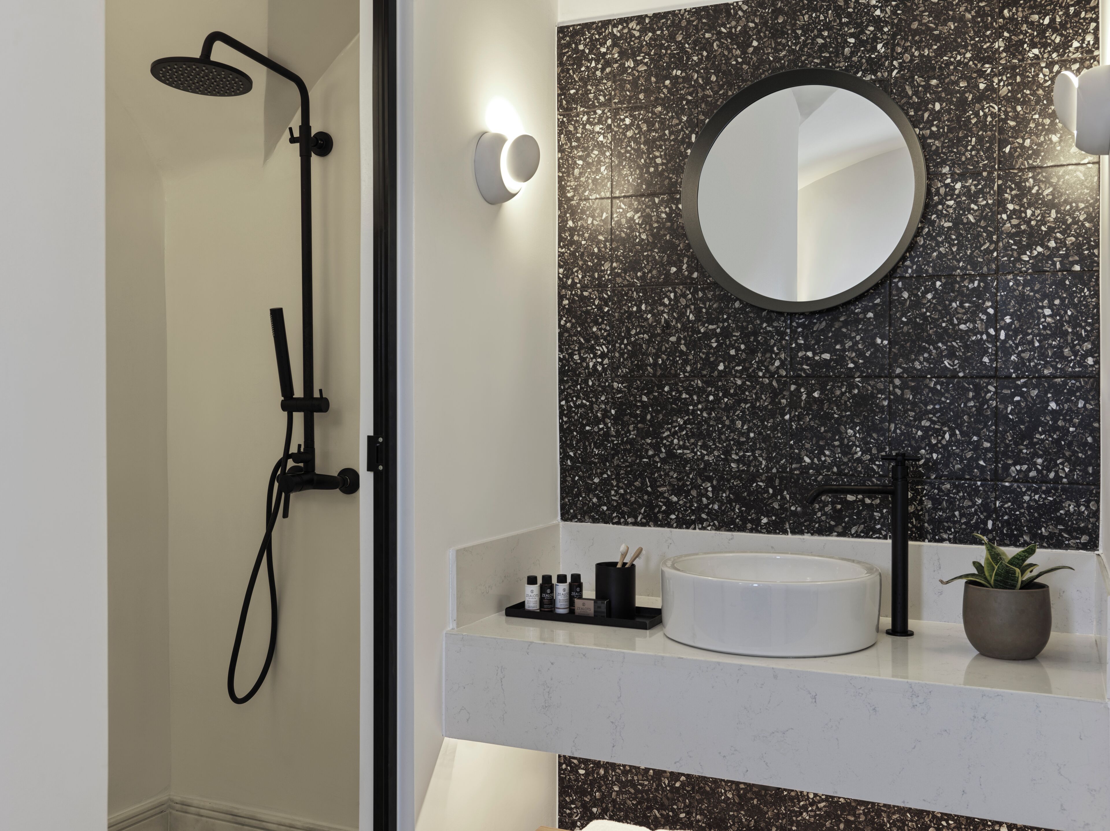 A modern bathroom with a shower, a round mirror, and a sink with toiletries.