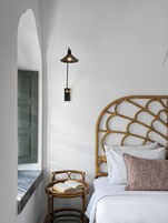 Un dormitorio con cama, una mesita de noche con un libro, una lámpara de pared y una ventana con vistas al exterior.