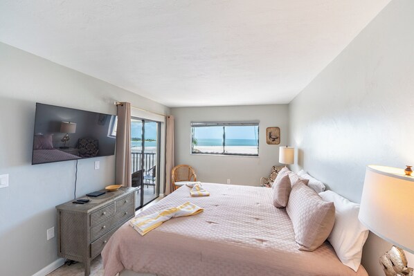 Un dormitorio con cama, televisor, ventana y vistas a la playa, además de un aparador.