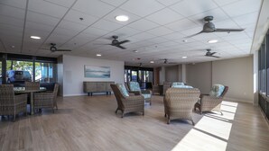 Een ruime binnenruimte met plafondventilatoren, rieten meubels en een groot raam dat natuurlijk licht binnenlaat.