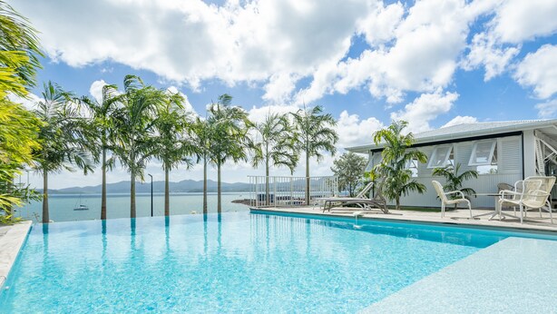 Une piscine d’eau cristalline, bordée de chaises longues et offrant une vue sur la mer.