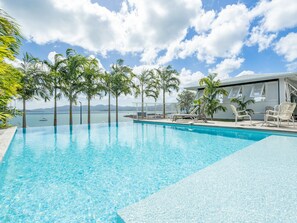 Une piscine d’eau cristalline, bordée de chaises longues et offrant une vue sur la mer.