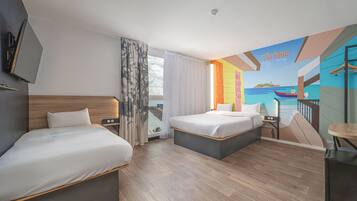 Habitación de hotel con dos camas, un ventanal con cortinas, un mural de una playa y una pequeña mesa con una silla.