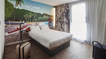 Una habitación de hotel con una cama, una maleta, una mesita de noche y un mural que representa una playa.