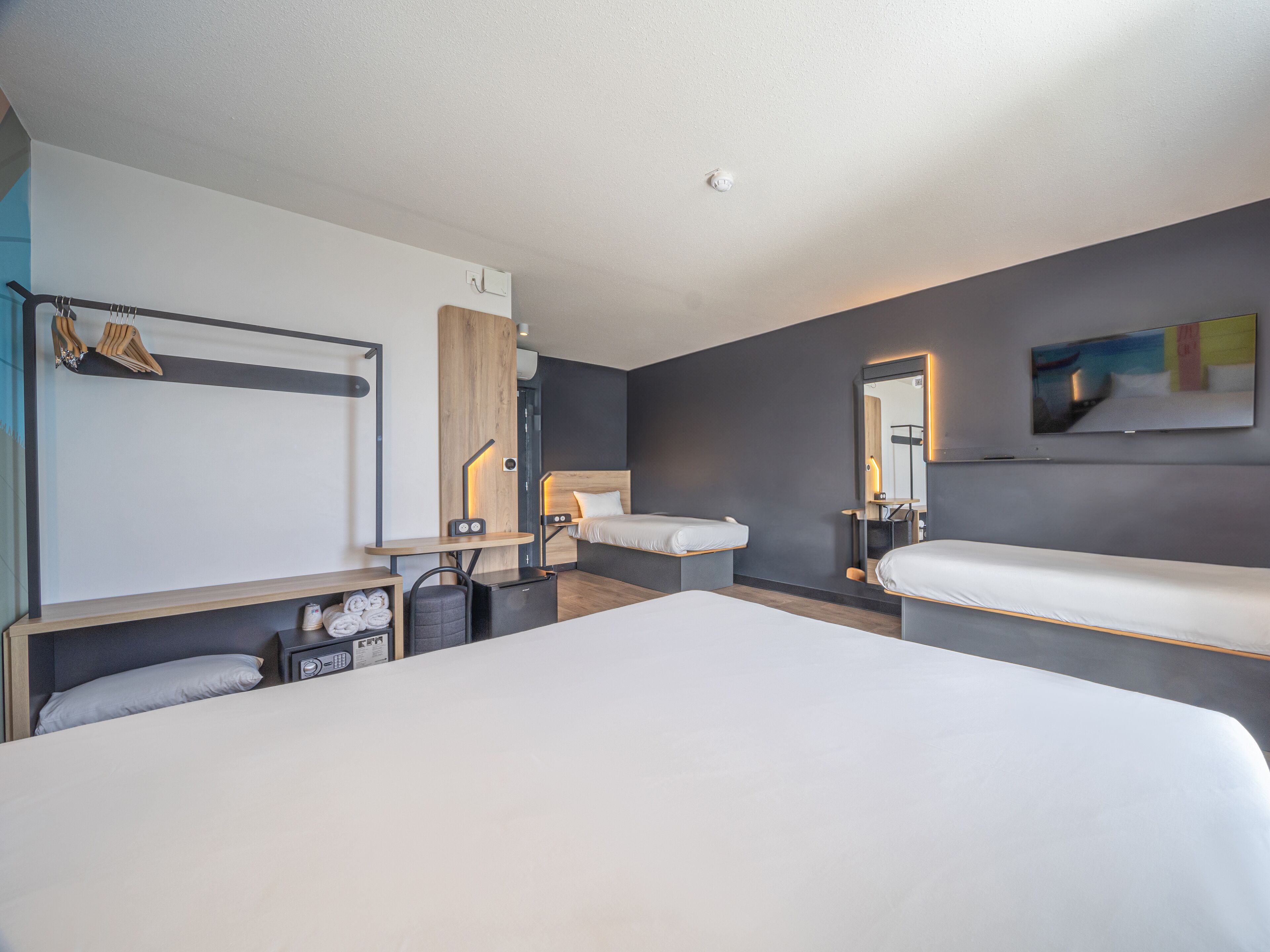 Une chambre d’hôtel moderne avec un grand lit, des tables de chevet, un miroir et un téléviseur.