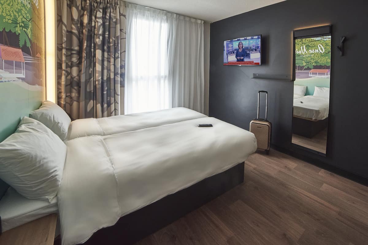 Une chambre d’hôtel avec un grand lit, un bureau, une chaise, une valise, une télévision et un miroir.