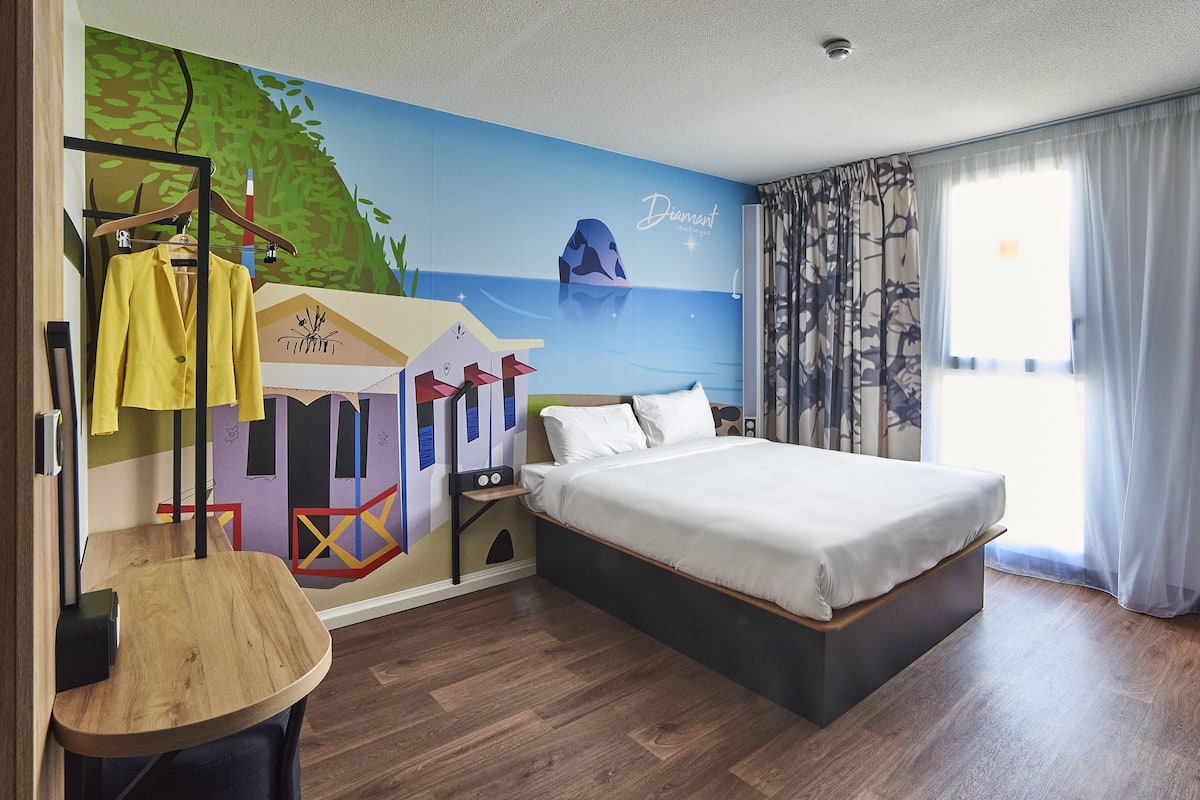 Une chambre d’hôtel avec un lit, une armoire, un miroir et une fresque murale.
