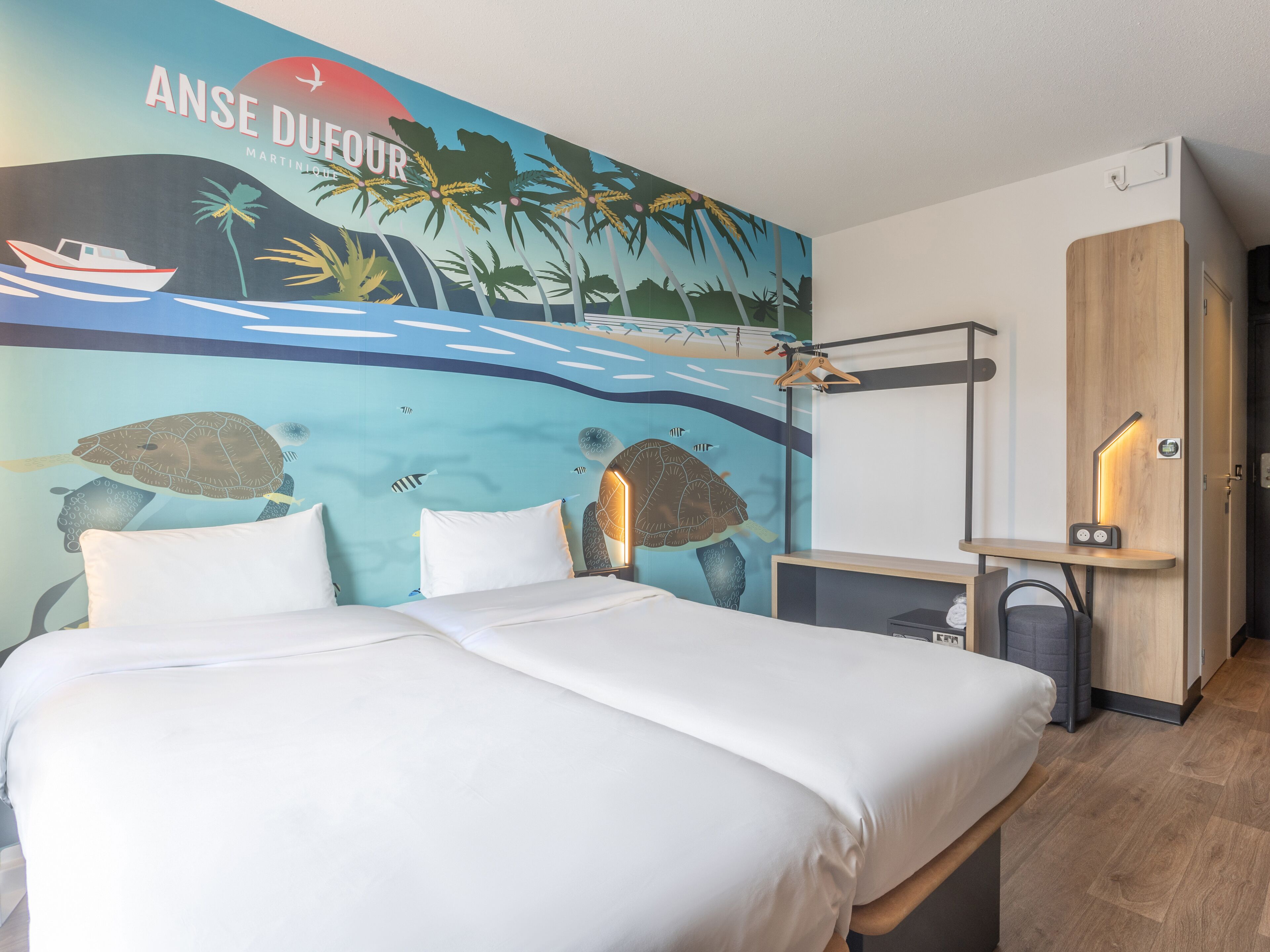 A hotel room with a mural of a tropical scene, a bed with white linens, a wooden nightstand, and a wardrobe.