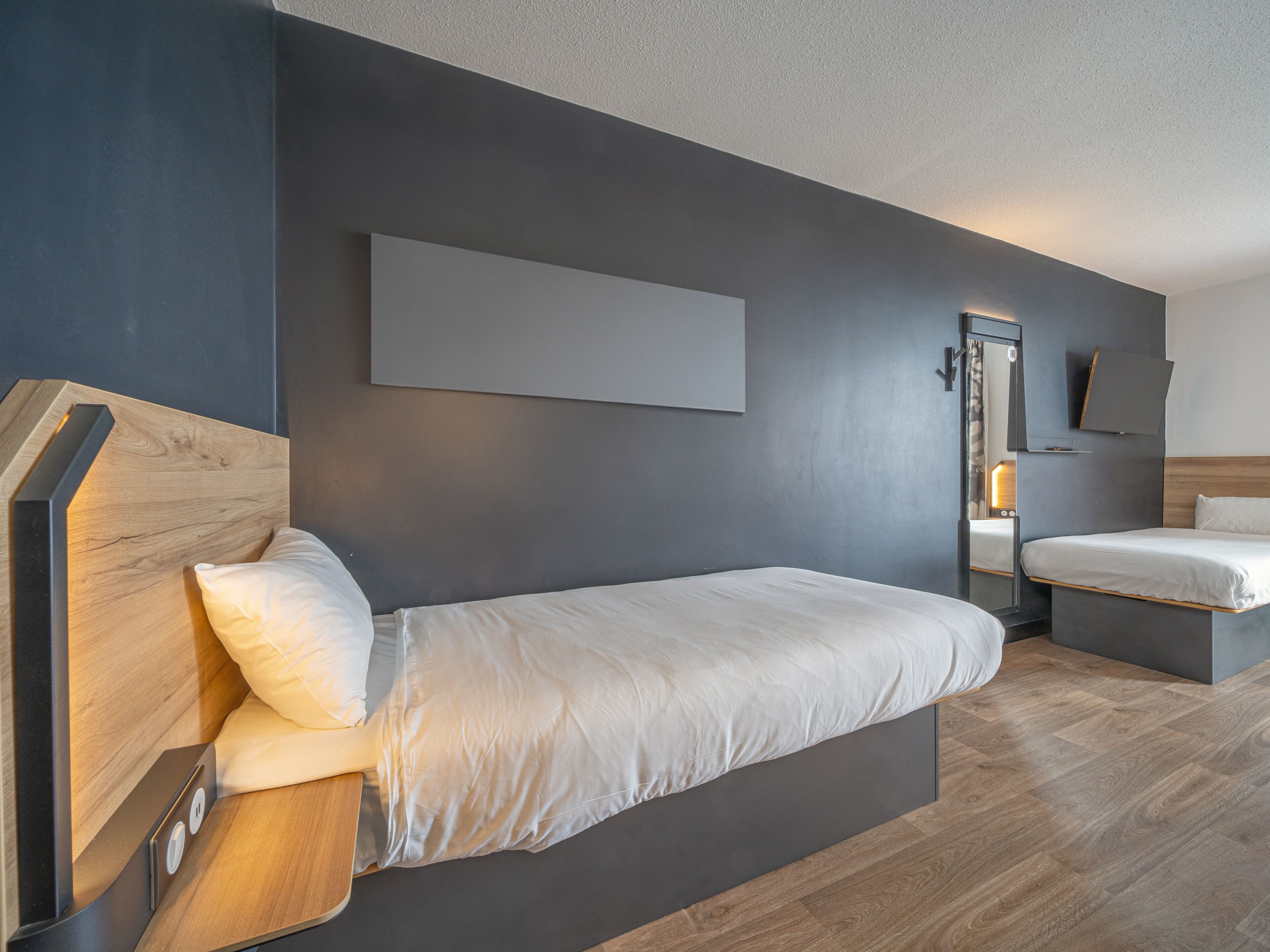 Une chambre d’hôtel moderne dotée d’un grand lit, d’une table de chevet, d’un téléviseur à écran plat fixé au mur et d’une tête de lit en bois.