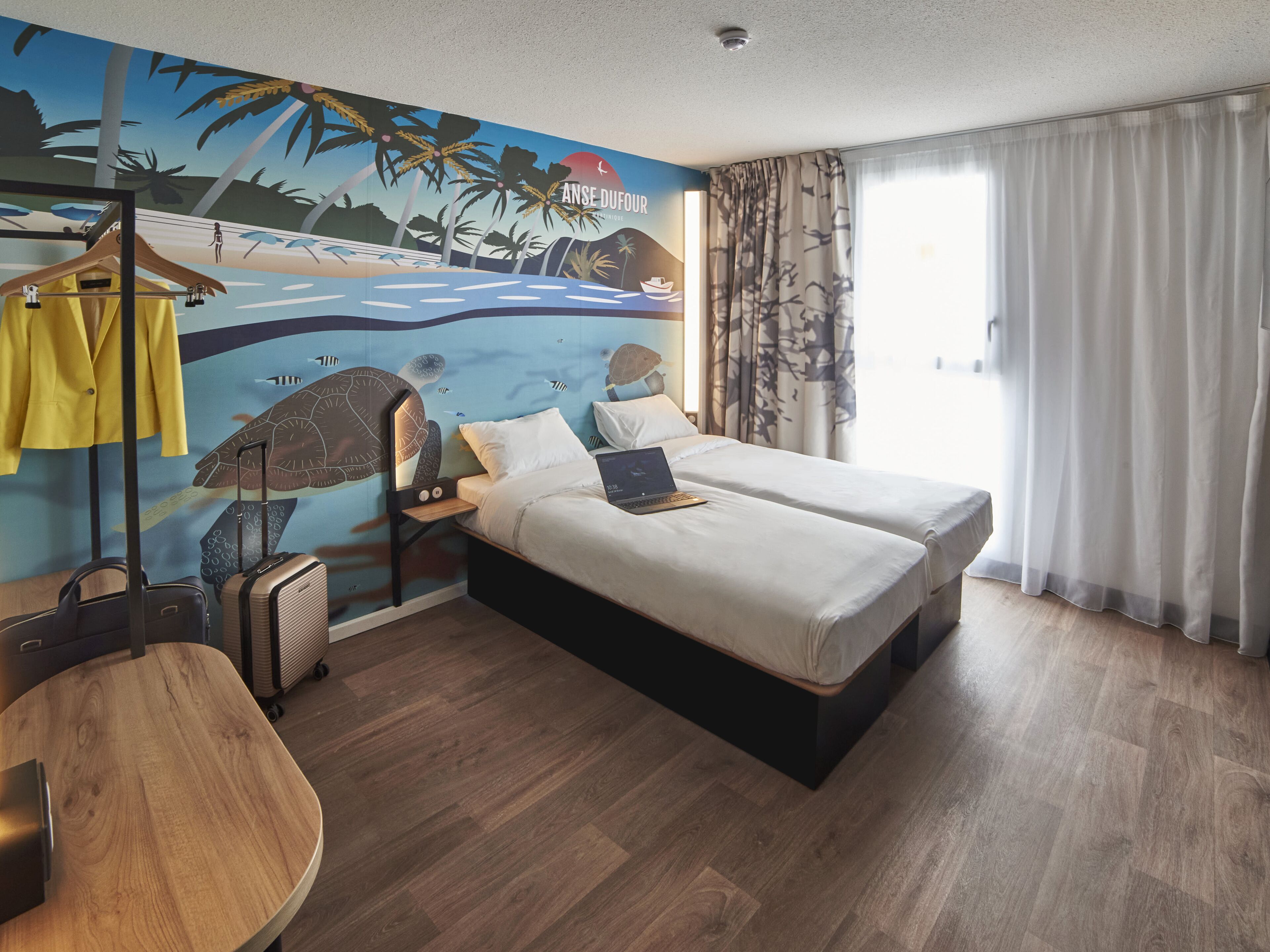 Habitación de hotel con cama, escritorio, silla, armario y un mural con una escena de playa.