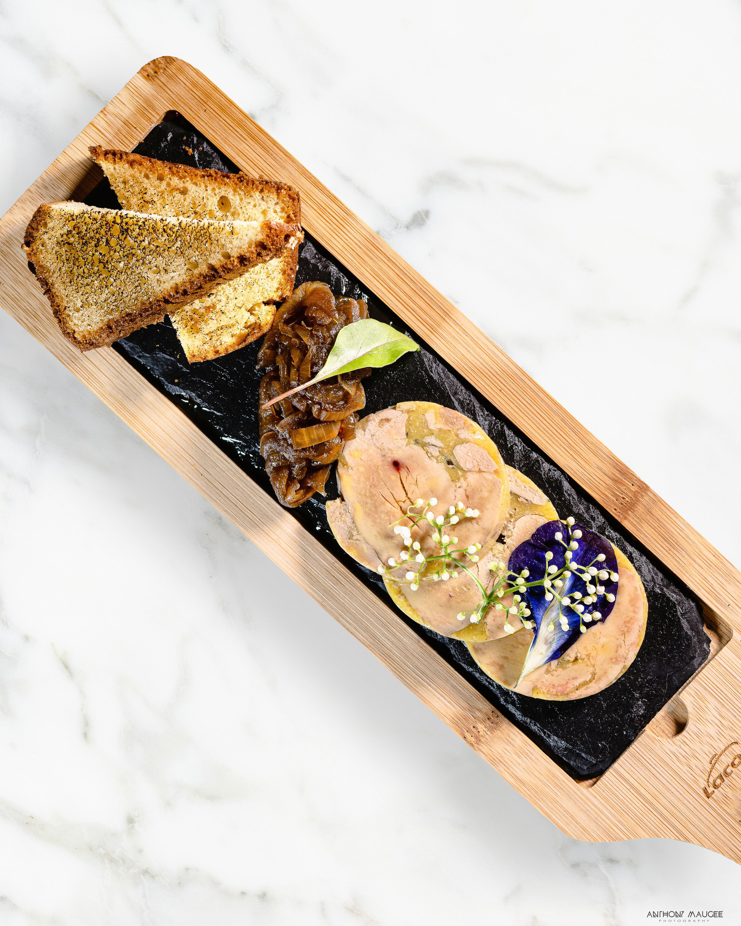 A wooden serving board with a variety of food items including bread, a meat dish, and a decorative element with flowers.