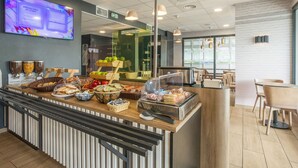 Un buffet de petit-déjeuner proposant une variété d’aliments, un menu numérique affiché sur un écran et un espace repas avec des tables et des chaises.