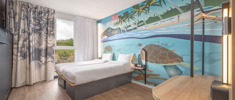 Un dormitorio con cama, una mesita, una silla, televisor y un mural con una playa.