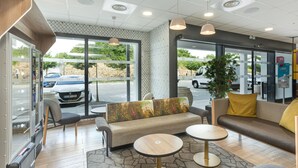 Un hall d’entrée moderne, doté d’un espace détente, d’un comptoir d’accueil et de grandes fenêtres donnant sur un parking.