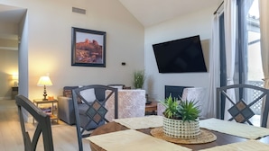 A dining area with a round wooden table, chairs, a potted plant, and a framed picture on the wall. - Near Spring Training! Snowbird Mesa Condo w/ Pool (Mesa)