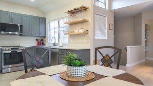A modern kitchen with grey cabinets, a stainless steel oven, and a microwave. There is a dining table with a woven placemat and a potted plant in the center. - Near Spring Training! Snowbird Mesa Condo w/ Pool (Mesa)