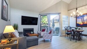 A spacious living room with a fireplace, a television mounted on the wall, and a dining area with a table and chairs. - Near Spring Training! Snowbird Mesa Condo w/ Pool (Mesa)