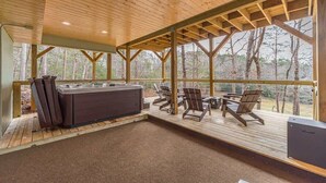 Un terrazzo in legno con una vasca idromassaggio, sedie e vista sulla foresta.