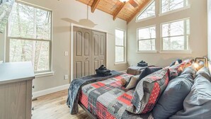 Una camera da letto con soffitto in legno, ampie finestre, un letto con copriletto e una porta.