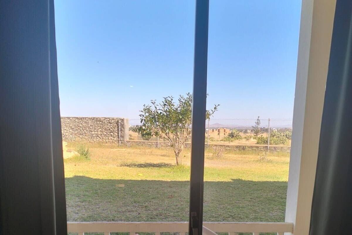 Vista de um quarto com porta de vidro deslizante para uma varanda, com uma cadeira de plástico branca e uma mesa pequena.