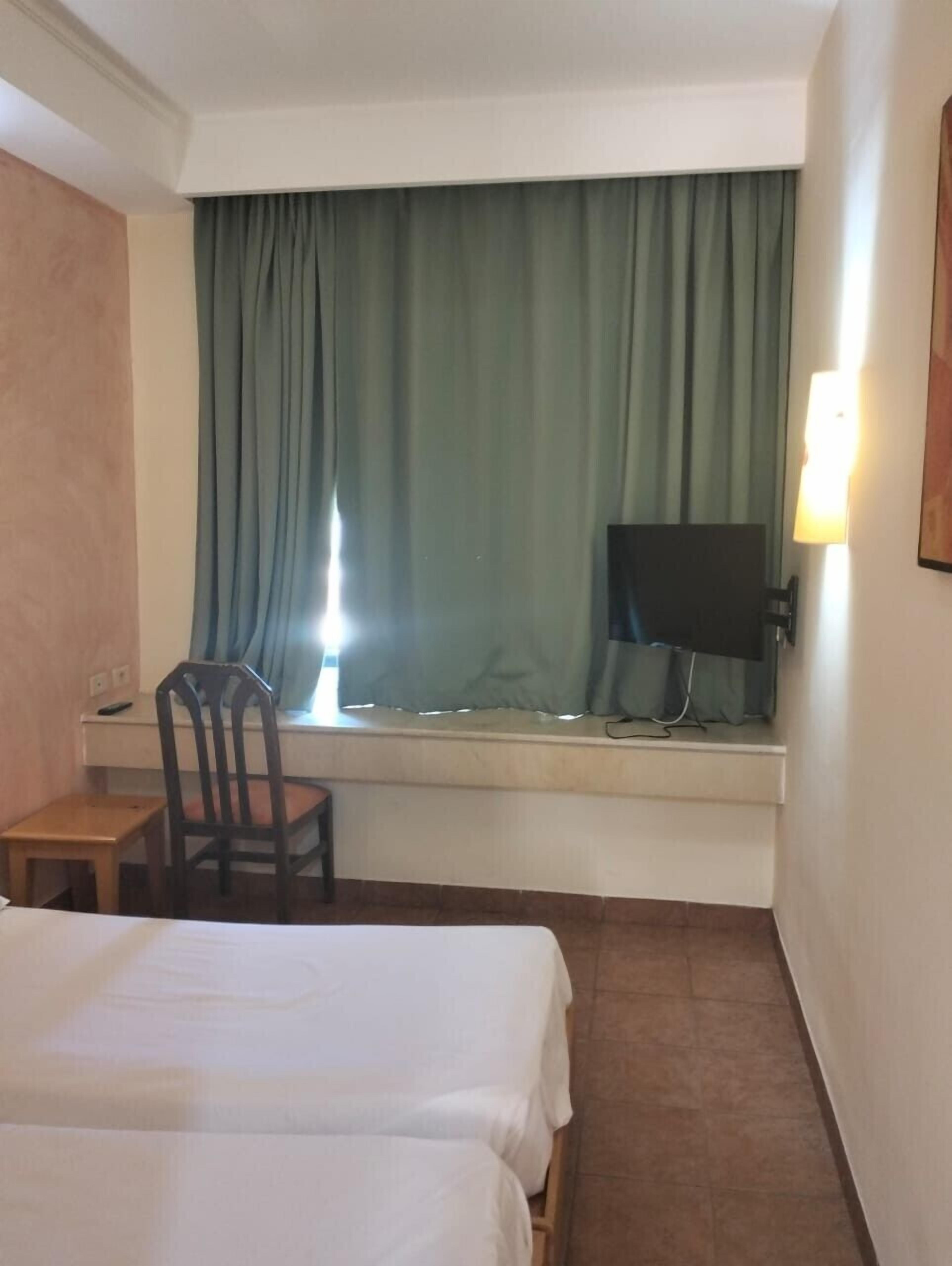 A hotel room with two beds, a desk with a chair, a TV, and a window with curtains.