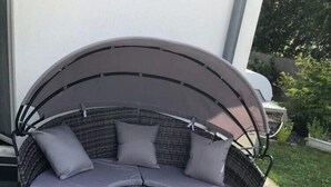 En stykke flettet hjørnesofa med puder og to matchende skraldebægre på en fliseterrasse.