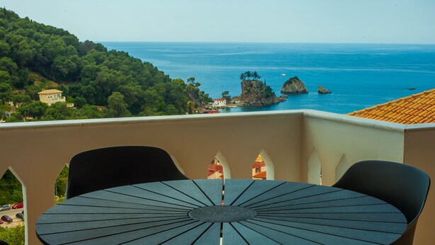 A round table with chairs on a balcony overlooking a coastal view with rocky outcrops and a clear sky. - Evgenias sea view apartments (Parga)