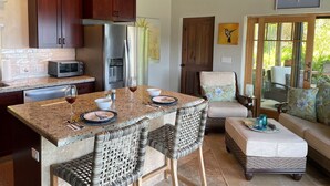 A kitchen with a granite countertop, stainless steel appliances, and a dining area with wicker chairs and a cushioned bench. - MandeVilla Cottage at Ixora spectacular views AC in bedroom mid island location. (St.John)