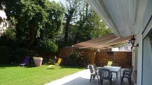 A patio with a tiled floor, a table, and chairs. There is a lawn and a wooden fence in the background. - Spacious apartment in villa with large private garden and terrace near the sea (Anglet)