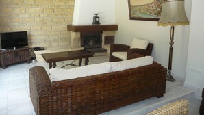 A living room with a brick wall, a fireplace, a sofa, a TV, and a lamp. - Spacious apartment in villa with large private garden and terrace near the sea (Anglet)