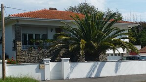 A two-story house with a stone facade, a tiled roof, and a large palm tree in the front yard. - Spacious apartment in villa with large private garden and terrace near the sea (Anglet)