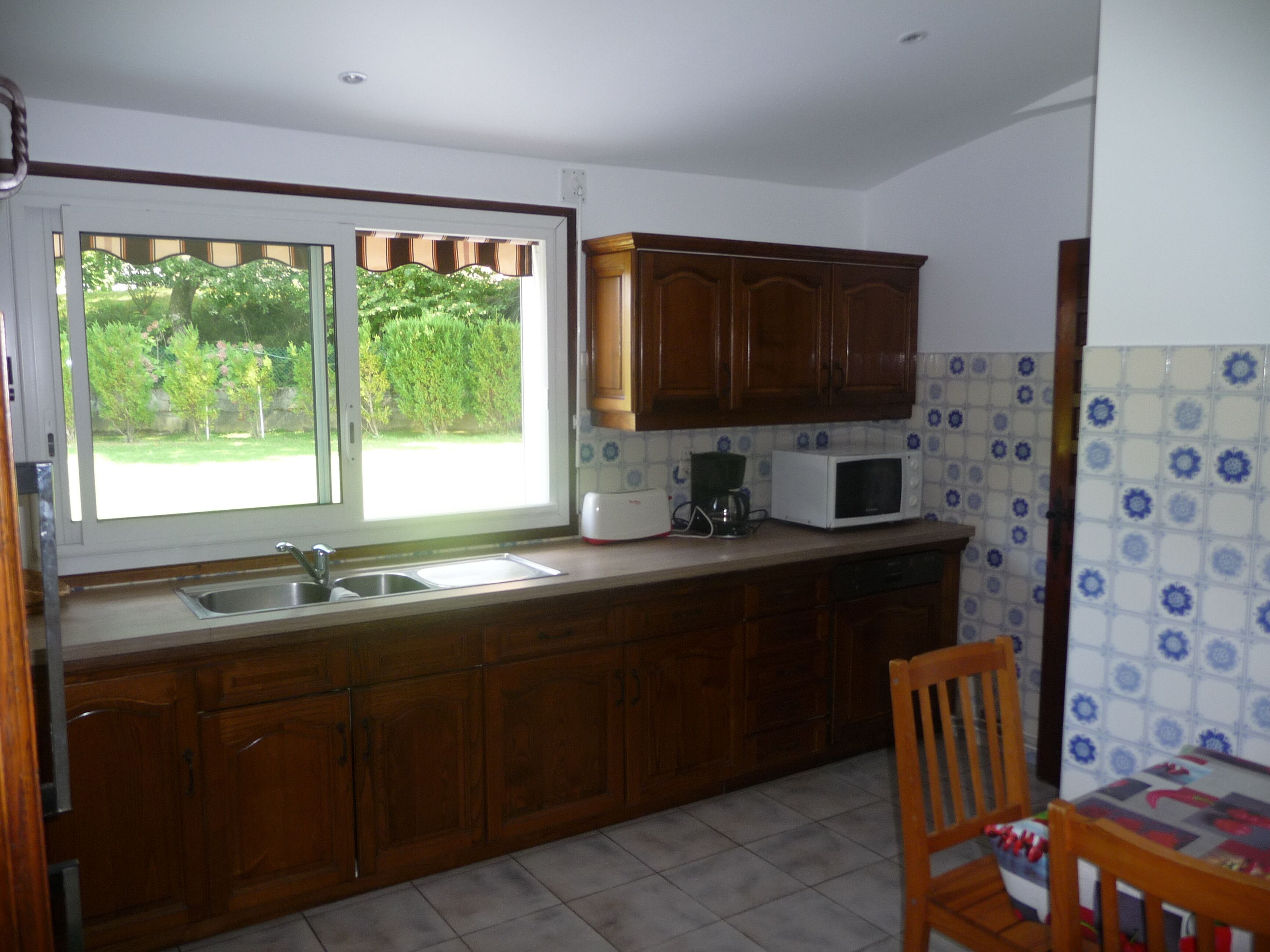 A kitchen with wooden cabinets, a microwave, a coffee maker, and a window with a view of greenery.